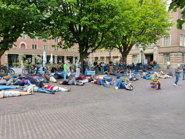 Mensen staan in kring en liggen op de grond voor dood om de gemeente te bewegen om de Klimaatnoodtoestand uit te roepen
